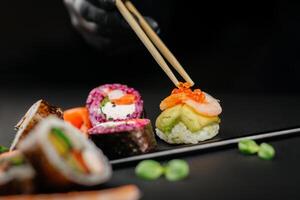 Hand halten Essstäbchen ein elegant Stück von Sushi beim Restaurant. Kalifornien rollen Sushi japanisch Essen Reis Ball. Vorderseite Sicht. kreativ japanisch Küche Konzept. hoch Qualität Foto