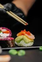 Hand halten Essstäbchen ein elegant Stück von Sushi beim Restaurant. Kalifornien rollen Sushi japanisch Essen Reis Ball. Vorderseite Sicht. kreativ japanisch Küche Konzept. hoch Qualität Foto