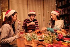 Freunde genießen es, am Tisch mit Spezialitäten zu essen, junge Frau, die im Speisesaal des Hauses gebratenen Truthahn schneidet, mit Ornamenten dekoriert, Weihnachtsfest und Neujahrsfeier. foto