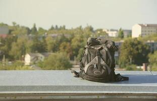 Der schwarze Rucksack liegt bei sonnigem Wetter auf dem Metallrand des Daches eines mehrstöckigen Wohngebäudes foto