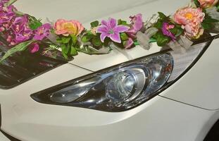 ein detailreiches Foto der Motorhaube des Hochzeitsautos, geschmückt mit vielen verschiedenen Blumen. Das Auto wird für eine Hochzeitszeremonie vorbereitet