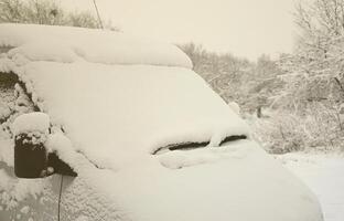 Fragment des Autos unter einer Schneeschicht nach einem starken Schneefall. Die Karosserie des Autos ist mit weißem Schnee bedeckt foto