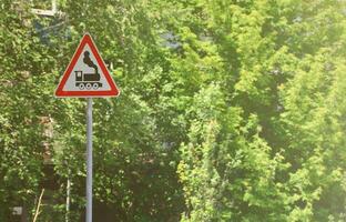 dreieckiges Straßenschild mit dem Bild einer schwarzen Lokomotive auf weißem Hintergrund in einem roten Rahmen. Warnzeichen für das Vorhandensein einer Eisenbahn, die die Autostraße kreuzt foto