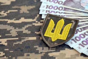 ukrainisch Heer Symbol und Bündel von Griwna Rechnungen auf Militär- Uniform. Zahlungen zu Soldaten von das ukrainisch Armee, Gehälter zu das Militär- foto