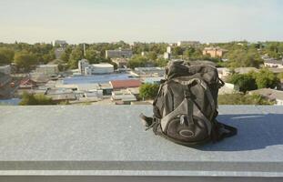 Der schwarze Rucksack liegt bei sonnigem Wetter auf dem Metallrand des Daches eines mehrstöckigen Wohngebäudes foto