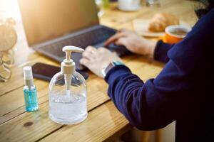 Frauen mit Laptop Arbeiten sauber Hände mit Alkohol und trinken Kaffee Tasse heiß im das Morgen foto