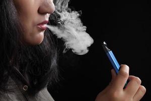 Nahaufnahme junge Frau raucht E-Zigarette auf schwarzem Hintergrund foto