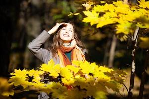 glückliche junge Frau im Sonnenschein unter gelbem Herbstlaub foto