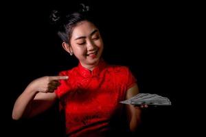 Porträt asiatische Frau rotes Kleid traditionelles Cheongsam hält Geld 100-US-Dollar-Scheine auf schwarzem Hintergrund