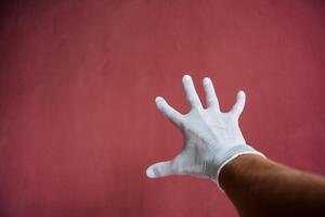 ein Hand im ein Weiß medizinisch Handschuh erstreckt sich nach vorne, ein verschwitzt Hand unter Latex, Finger Verbreitung aus gegen ein kastanienbraun Wand, Hand Schutz foto