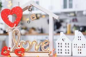 Schlüssel zu winzig Haus von gemütlich Zuhause mit Valentinstag Dekor auf Tabelle von Küche. Geschenk zum Valentinsgrüße Tag, Familie Liebe Nest. Design, Projekt, ziehen um zu Neu Haus, Hypothek, Miete und Kauf echt Nachlass foto