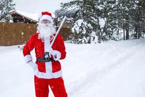 Santa claus reinigt Schnee mit Schaufel im Winter draußen nach ein Schneefall. Reinigung das Straßen im das Dorf, Clearing das Passage zum Autos, schwierig Wetter Bedingungen zum Weihnachten und Neu Jahr foto