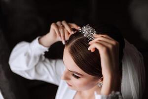 ein schön Brünette Braut mit ein Tiara im ihr Haar ist bekommen bereit zum das Hochzeit im ein schön Kleid im Boudoir Stil. Nahansicht Hochzeit Porträt, Foto. foto