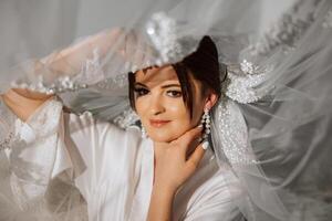 ein schön Brünette Braut mit ein Tiara im ihr Haar ist bekommen bereit zum das Hochzeit im ein schön Kleid im Boudoir Stil. Nahansicht Hochzeit Porträt, Foto. foto