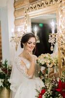 elegant Brünette Braut posiert im ein Weiß Kleid in der Nähe von das Spiegel. Porträt von das Braut, Hochzeit bilden und Frisur, Hochzeit Mode. schön Braut im ein Schleier. foto