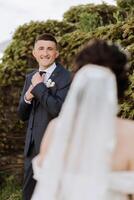 ein schön jung Braut im ein Sommer- Park ist Gehen zu ihr Bräutigam. Foto von das Bräutigam im ein Blau Anzug. selektiv Fokus. schön Hochzeit Weiß Kleid. Spaziergänge im das Park. ein glücklich und liebend Paar.