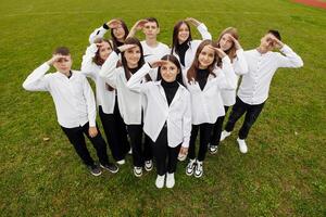 ein Gruppe von viele glücklich Jugendliche gekleidet im das gleich Outfit haben Spaß und posieren im ein Stadion in der Nähe von ein Hochschule. Konzept von Freundschaft, Momente von Glück. Schule Freundschaft foto