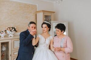 glücklich Eltern halt das Hände von das Braut Wer ist bekommen verheiratet und Unterstützung ihr, tragen ein Hochzeit Kleid und ein lange Schleier. foto