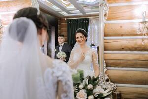 elegant Brünette Braut posiert im ein Weiß Kleid in der Nähe von das Spiegel. Porträt von das Braut, Hochzeit bilden und Frisur, Hochzeit Mode. schön Braut im ein Schleier. foto