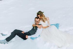 jung Mann und Frau Laufen Lügen auf Schnee, Lachen, täuschen um, haben Spaß spielen Schneebälle. europäisch Winter Hochzeit foto