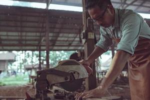 Zimmermann schneidet Holz mit einer Kettensäge, um an seiner Holzbearbeitung zu arbeiten. foto