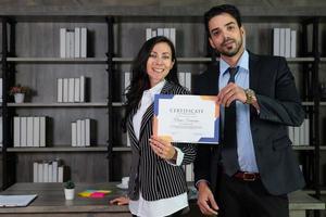 Junge kaukasische Geschäftsfrau und arabischer Geschäftsmann erhalten ein Zertifikat für das neue Projektdesign und zeigen es im Büro foto