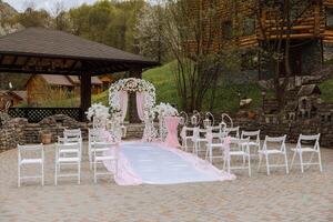 Hochzeit Dekor. viele Weiß Stühle und ein Weiß Weg. ein Weiß und Rosa Bogen dekoriert mit Blumen. Vorbereitung zum das Hochzeit Zeremonie. Feier foto