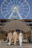 drei schön jung Teenager Mädchen haben Spaß zusammen draußen gegen das Hintergrund von ein Ferris Rad im ein Italienisch Stadt. städtisch Lebensstil. Stadt Center. Beste freunde im beiläufig Kleidung. foto