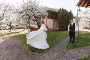 das Braut ist kreisen im ihr Hochzeit Kleid, und das Bräutigam ist suchen beim ihr. Hochzeit Foto Session im ein schön Frühling Park.