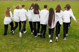 ein Gruppe von viele glücklich Jugendliche gekleidet im das gleich Outfit haben Spaß und posieren im ein Stadion in der Nähe von ein Hochschule. Konzept von Freundschaft, Momente von Glück. Schule Freundschaft foto