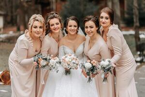 ein Brünette Braut im ein Weiß elegant Kleid und ihr freunde im grau Kleider Pose mit Blumensträuße. Hochzeit Porträt im Natur, Hochzeit Foto im Licht Farben.