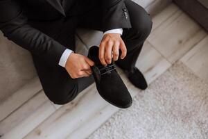 ein elegant Mann trägt schwarz Leder formal Schuhe. binden Schuhe. Geschäft Mann binden Schnürsenkel auf das Boden. oben schließen das Bräutigam ist vorbereiten zum das Hochzeit. foto