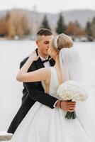 Hochzeit Porträt. das Braut im ein elegant lange Kleid, halten ein Strauß, und das Bräutigam im ein klassisch Anzug, Stand umarmen im das Winter Garten. foto