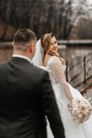 das Braut und Bräutigam sind Gehen in der Nähe von das Hotel und posieren, glücklich und genießen das Tag, halten Hände. ein lange Zug auf das Kleid. Winter Hochzeit foto