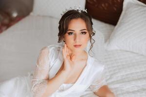 ein schön Brünette Braut mit ein Tiara im ihr Haar ist bekommen bereit zum das Hochzeit im ein schön Kleid im Boudoir Stil. Nahansicht Hochzeit Porträt, Foto. foto