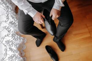 ein elegant Mann trägt schwarz Leder formal Schuhe. binden Schuhe. Geschäft Mann binden Schnürsenkel auf das Boden. oben schließen das Bräutigam ist vorbereiten zum das Hochzeit. foto