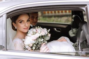 ein schön Braut, Sitzung im ein Auto, sieht aus aus von das öffnen Fenster von das Wagen. ein schön Braut mit ein Strauß von Blumen im ihr Hände ist Sitzung im ein stilvoll teuer Wagen. foto