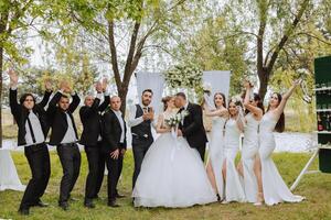 in voller Länge Porträt von das Jungvermählten und ihr freunde beim das Hochzeit. das Braut und Bräutigam mit Brautjungfern und freunde von das Bräutigam sind haben Spaß und Jubel beim das Hochzeit. foto