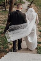 Porträt. das Braut im ein elegant lange Kleid und das Bräutigam sind umarmen und posieren im das Hof, Stehen auf ein Stein Weg. Hochzeit im Natur foto
