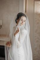 Mode Porträt von ein schön Braut im ein luxuriös Hochzeit Kleid mit Spitze und Kristalle im ein Arabisch Innere Stil. ein schön Braut unter ein Schleier. Vorbereitung zum das Hochzeit Zeremonie. foto