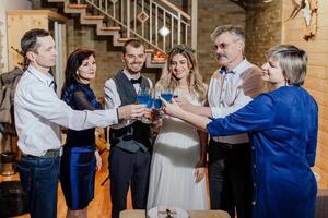 das Braut und Bräutigam feiern ihr Hochzeit mit ihr Eltern im ein hölzern Haus im das Berge. modern Hochzeit. Sie angehoben ihr Brille. foto