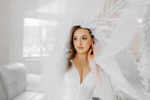 Porträt von ein zärtlich Braut im ein Hochzeit Kleid und ein schön Frisur unter ein Schleier im ihr Zimmer von das Morgen foto
