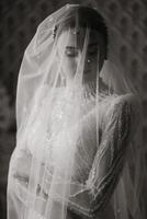 Hochzeit schwarz und Weiß Porträt. das Braut im ein elegant Hochzeit Kleid posiert eingewickelt im ein Schleier. Morgen von das Braut. schön Haar und bilden foto