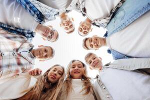 groß Gruppe von lächelnd jung Menschen Stehen, umarmen, suchen beim Kamera. Gruppe von heiter Teenager Menschen im ein Kreis suchen runter. niedrig Anzeigen Winkel. Kopieren Raum. foto