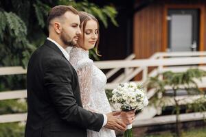 das schön Braut sanft Umarmungen das Bräutigam, Wer Umarmungen ihr durch das Schultern. Hochzeit Konzept. das Schönheit und Zärtlichkeit von ein Mann und ein Frau foto