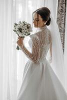 Mode Porträt von ein schön Braut im ein luxuriös Hochzeit Kleid mit Spitze und Kristalle im ein Arabisch Innere Stil. schön Braut mit ein Strauß von Blumen. Vorbereitung zum das Hochzeit Zeremonie. foto
