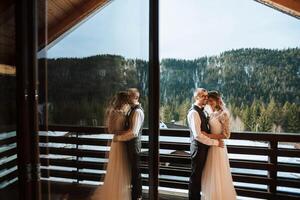 das Bräutigam umarmt das Braut gegen das Hintergrund von schneebedeckt Berge. ein Hochzeit Paar ist feiern ein Hochzeit im das Berge im Winter. foto