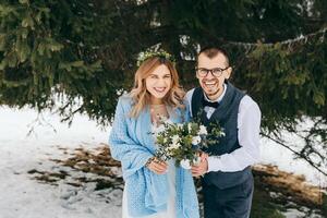 Winter Hochzeit im das Berge. Porträt von ein glücklich und lächelnd Braut und Bräutigam gegen das Hintergrund von ein Winter Wald. schön Braut und Bräutigam zärtlich umarmen. modern Winter Hochzeit. foto