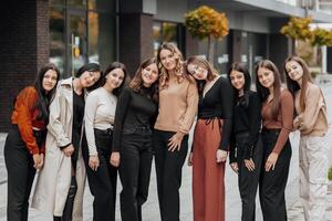 Gruppe von lächelnd und glücklich Teenager freunde tragen beiläufig Kleider Ausgaben Zeit zusammen, posieren und reden mit jeder andere in der Nähe von Hochschule Gebäude auf Herbst Tag. foto