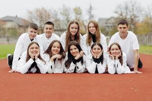 ein Gruppe von viele glücklich Jugendliche gekleidet im das gleich Outfit haben Spaß und posieren im ein Stadion in der Nähe von ein Hochschule. Konzept von Freundschaft, Momente von Glück. Schule Freundschaft foto